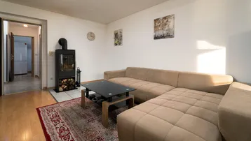 Gemütliches Wohnzimmer mit Ecksofa, Holzboden und einem modernen Holzofen.