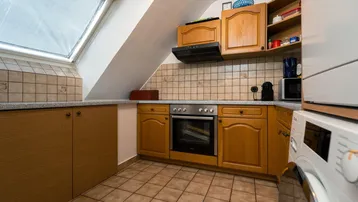 Küche im Dachgeschoss mit Holzschränken, Einbauherd und Waschmaschine unter der Schräge.