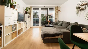 Helles Wohn-Esszimmer mit Parkettboden, großem Sofa und Zugang zum Balkon.