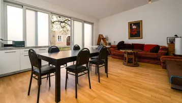 Geräumiger Wohn-Essbereich mit Holzboden, großen Fenstern und Zugang zum Innenhof.
