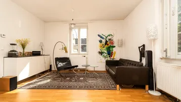 Helles Wohnzimmer mit Parkettboden, bequemen Ledermöbeln und einem farbenfrohen Kunstwerk an der Wand.