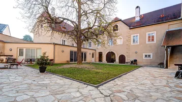 Historischer Innenhof mit altem Baumbestand, Steinplatten und Sitzgelegenheiten, umgeben von Gebäuden.