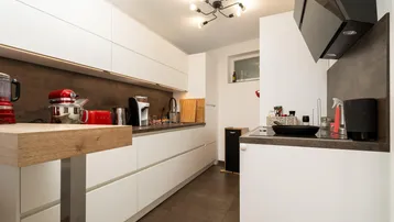 Helle, moderne Küche mit weißen Fronten, dunkler Arbeitsplatte und Holzakzenten.