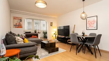 Helles Wohn- und Esszimmer mit Parkettboden, bequemer Couch und modernem Esstisch.