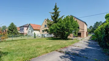 Blick auf das Mehrfamilienhaus mit großem Grundstück und angrenzender Straße an einem sonnigen Tag.