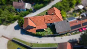 Luftaufnahme eines Hauses mit rotem Ziegeldach, umgeben von grüner Landschaft und Straßen.