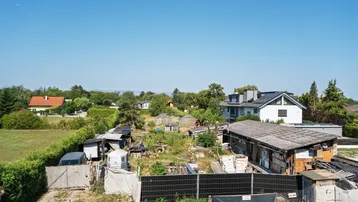 Weitläufige Ansicht der Umgebung mit Häusern, Gärten und viel Grün unter blauem Himmel.