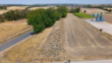 Luftaufnahme eines ländlichen Grundstücks mit Feldern, einer Straße und Bäumen im Hintergrund.