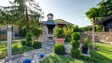 Gepflegter Gartenbereich mit gemauertem Grillplatz und dekorativen Pflanzen unter strahlender Sonne.