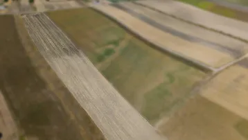 Luftaufnahme einer ländlichen Landschaft mit weiten Feldern und einem kleinen Dorf im Hintergrund, das die Umgebung zeigt.