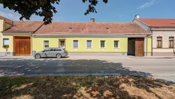 Ländliches Haus mit gelber Fassade, rotem Ziegeldach und einem Auto davor an der Straße.