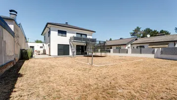 Hinteransicht des Hauses mit großem Gartenbereich und Trampolin unter blauem Himmel.