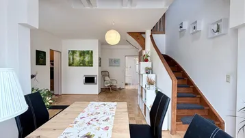 Geräumiger Wohn- und Essbereich mit Holzboden, Kamin und offener Holztreppe zum Obergeschoss.