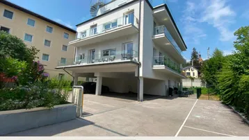 Modernes Mehrfamilienhaus mit Balkonen und Tiefgaragenzufahrt unter blauem Himmel.
