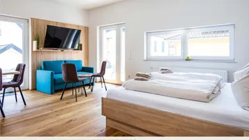 Helles Schlafzimmer mit Holzboden, einem Doppelbett und einem kleinen Sitzbereich mit Fernseher.