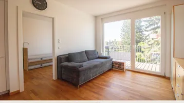 Helles Wohnzimmer mit Holzboden, gemütlichem Sofa und Zugang zu einem Balkon.