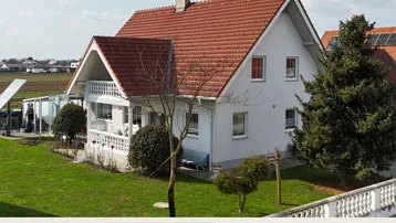 Haus mit rotem Ziegeldach, weißer Fassade und gepflegtem Vorgarten in ländlicher Umgebung.