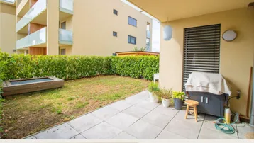 Geräumige Terrasse mit gepflastertem Bereich, kleinem Rasen und Blick auf die Wohnanlage.