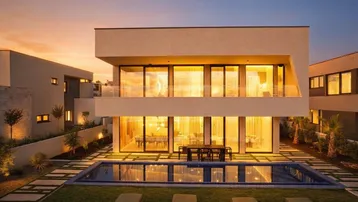 Moderne Villa mit großem Pool, weitläufigem Garten und beleuchteten Innenräumen bei Sonnenuntergang.