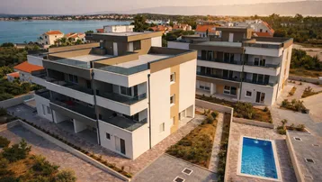 Moderne Apartmentgebäude mit Flachdächern, Balkonen und Meerblick, umgeben von mediterraner Landschaft und einem Pool.