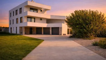 Moderne weiße Villa mit klarer Architektur, großzügiger Auffahrt und integrierten Garagen, umgeben von Grünflächen.