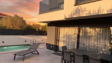Große Terrasse mit Esstisch, Sonnenliege und privatem Pool bei Sonnenuntergang.