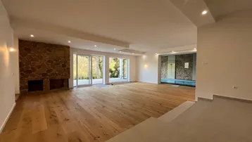 Großzügiger Wohnbereich mit Steinkamin, Holzparkett und Zugang zum Innenpoolbereich.