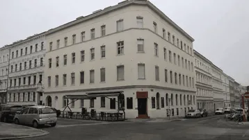 Eckgebäude mit mehreren Etagen und einem Café im Erdgeschoss an einer städtischen Straße.