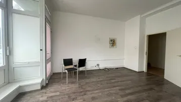 Geräumiger, heller Wohnraum mit dunklem Laminatboden und großem Fensterbereich.