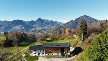 Ländliches Anwesen mit traditionellem Bauernhaus und Nebengebäude vor beeindruckender Bergkulisse.