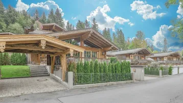 Traditionelle Holzchalets mit Carport, Balkonen und Blick auf die bewaldeten Berge unter blauem Himmel.