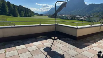 Große Dachterrasse mit Fliesenboden und weitem Blick auf die umliegende Landschaft und Berge.