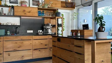Moderne Küche mit Holzelementen, Kücheninsel und Blick ins Grüne durch große Fenster.