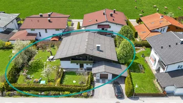 Luftaufnahme eines Hauses mit Garten und umliegender grüner Landschaft, umrandet von einem Kreis.