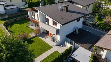 Luftaufnahme eines modernen Einfamilienhauses mit weißer Fassade, dunklem Dach und gepflegtem Gartenbereich.