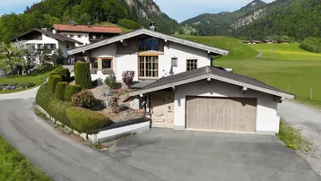 Traditionelles Haus im alpenländischen Stil mit Garage und gepflegter Außenanlage in grüner Umgebung.