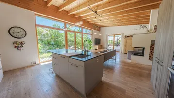 Moderne offene Küche mit Kochinsel, Holzbalkendecke und Blick in den Garten.