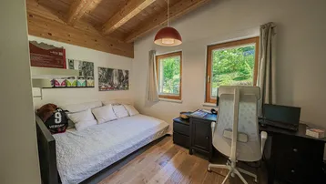 Helles Schlafzimmer mit Holzbalkendecke, Schreibtisch und Blick ins Grüne.