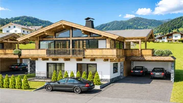 Modernes Chalet mit Holzfassade, großen Fenstern, Balkonen und Bergblick in alpiner Umgebung.