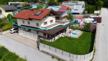 Luftaufnahme eines modernen Einfamilienhauses mit rotem Ziegeldach, gepflegtem Garten und kleinem Poolbereich.