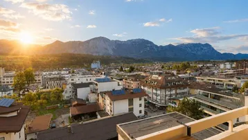 Balkon mit Holztisch und atemberaubendem Blick auf die Berge und die Stadt bei Sonnenuntergang.