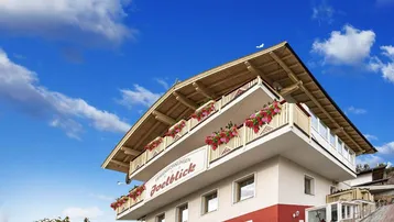 Modernes Gebäude im alpinen Stil mit blühenden Balkonen unter blauem Himmel.