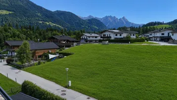 Blick auf eine Wohnsiedlung mit grünen Wiesen und majestätischen Bergen im Hintergrund.