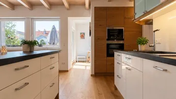 Helle, moderne Küche mit Holzbalkendecke, weißen Schränken und dunkler Arbeitsplatte.