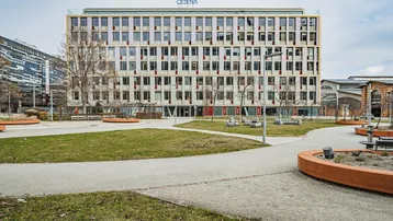 Modernes Bürogebäude mit vielen Fenstern und einem gepflegten Parkbereich davor.