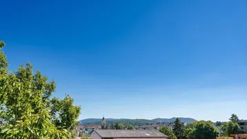 Weitläufiger Blick über die Stadt und die umliegende grüne Landschaft mit Bergen im Hintergrund.