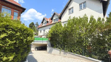 Mehrere Gebäude mit gepflasterter Auffahrt und grüner Bepflanzung unter blauem Himmel.