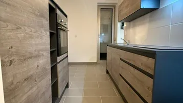 Moderne, schmale Küche mit Holzoptik-Fronten, integrierten Geräten und Fliesenboden.