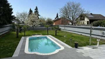 Großer Garten mit Swimmingpool und gepflegter Rasenfläche, umgeben von Bäumen und einem Zaun.