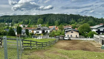 Panoramablick auf eine ländliche Siedlung mit Häusern, grünen Hügeln und Feldern unter bewölktem Himmel.